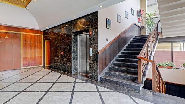 En moderne hotellobby med marmorgulv, en træreception, en trappe og en indbygget elevator.