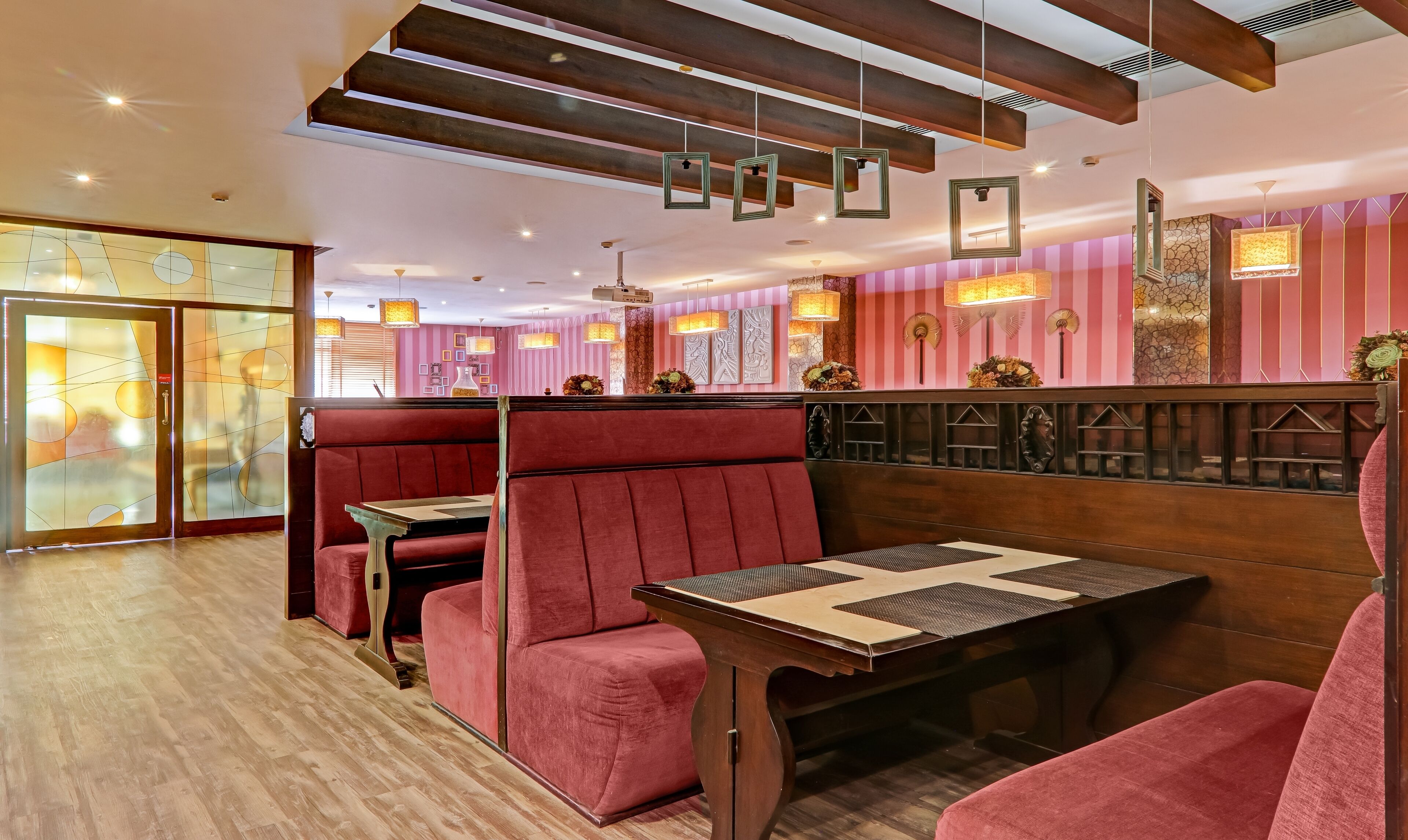 A restaurant interior with wooden tables and red upholstered booths, featuring striped walls and pendant lighting.