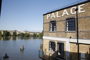 A building with the word "PALACE" on its facade, a river in the background, and a wooden deck in the foreground.