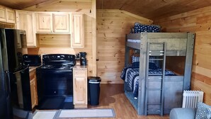A cozy cabin interior with a kitchen, a bunk bed, and a gray sofa.