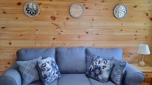 A grey sofa with floral cushions, a colorful striped rug, and decorative wall plates against a wooden wall.