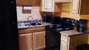 A compact kitchen with wooden cabinets, a black refrigerator, a stove, and a sink.
