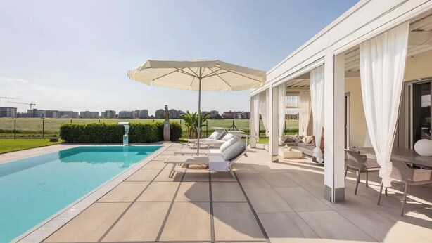 Un espace piscine extérieur moderne offrant une vue dégagée sur le paysage environnant, un coin salon couvert avec des parasols et une pelouse bien entretenue.