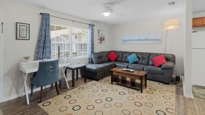 Un salon avec un canapé gris, une petite table, une chaise bleue et un tapis à motifs.