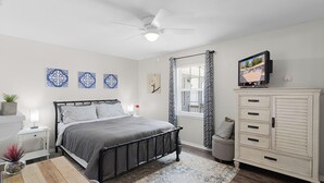 Une chambre à coucher comprenant un lit, une table de chevet, un téléviseur, une armoire et une fenêtre avec des rideaux.