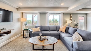 A living room with a sectional sofa, a coffee table, and a flat-screen TV. - Grandview Hideaway - Vast views, walk to restaurants, disk golf, lots of privacy (Erie)