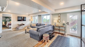A spacious living room with a grey sofa, a coffee table, and a TV mounted on the wall. - Grandview Hideaway - Vast views, walk to restaurants, disk golf, lots of privacy (Erie)