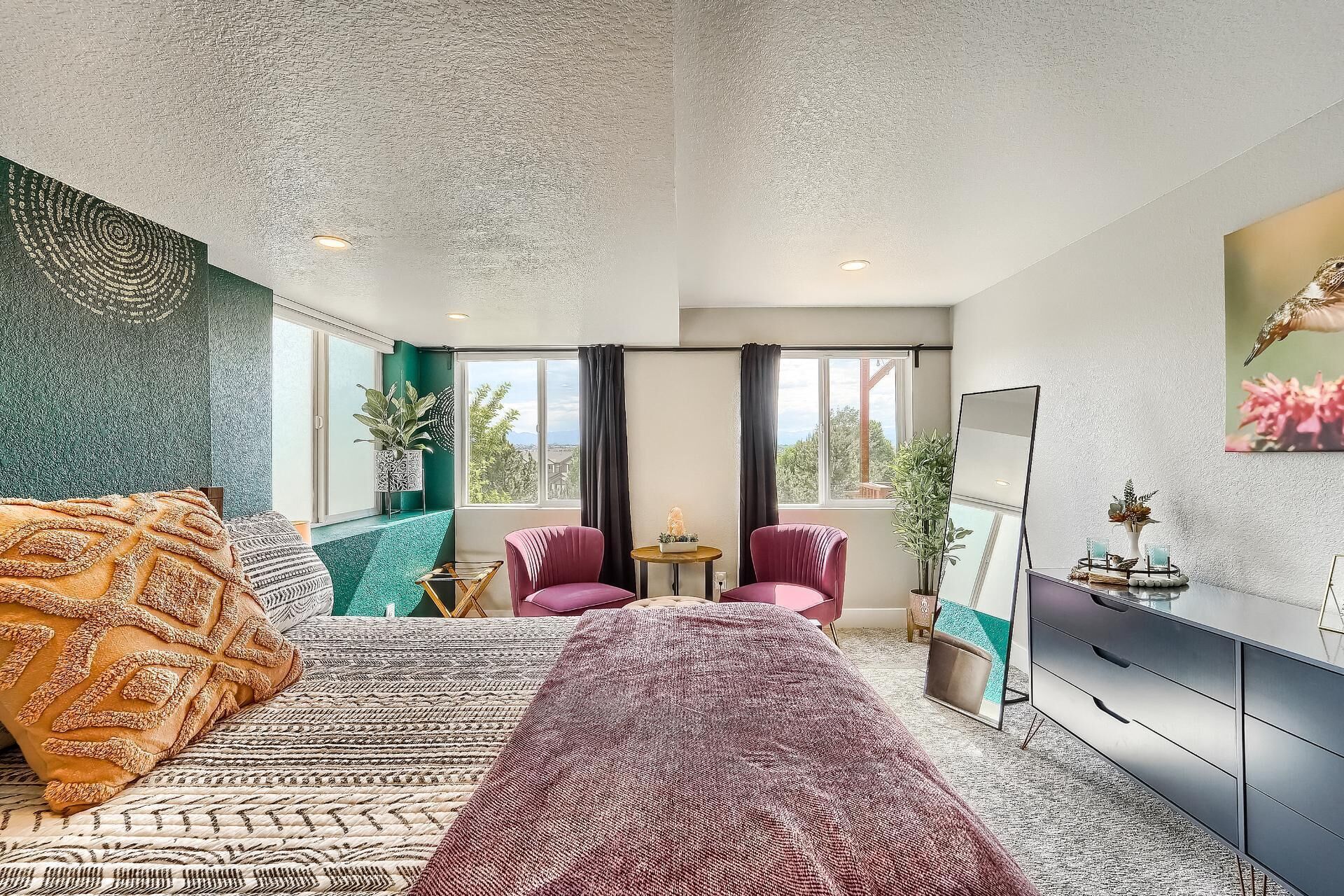 A modern bedroom with a large bed, two chairs, a small table, and a dresser.