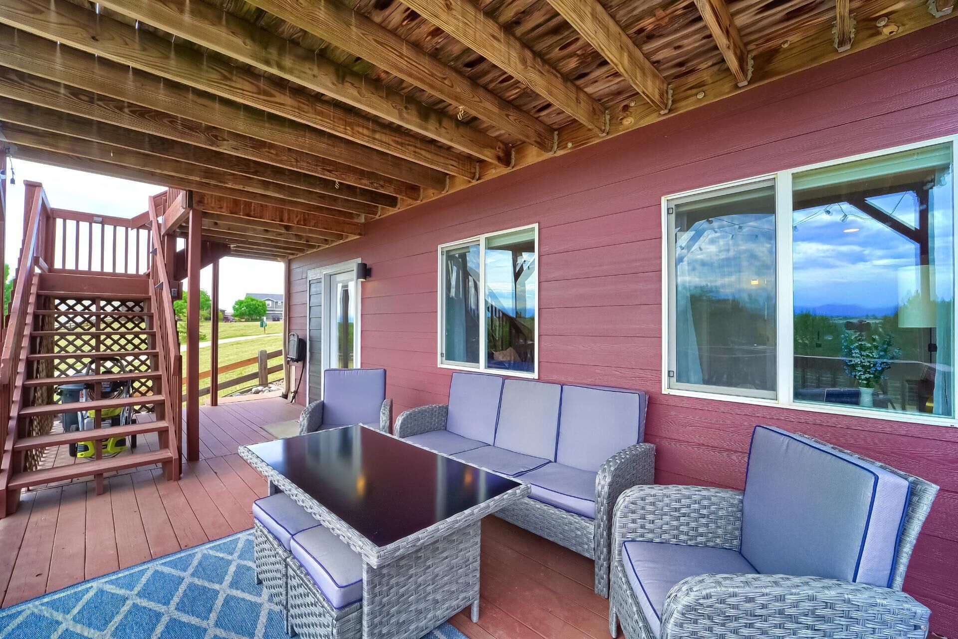 A covered patio with wicker furniture, a table, and a wooden staircase.