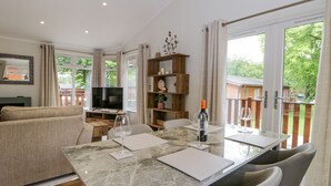 A modern living room with a sofa, a TV, a dining table with chairs, and a balcony with a wooden railing. - Kirkstone Lodge (Windermere)