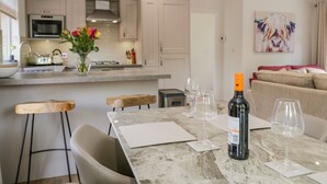 A modern kitchen with a dining area, featuring a marble table, chairs, and a wine bottle. - Kirkstone Lodge (Windermere)