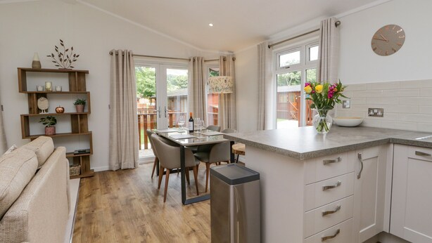 A modern kitchen with a dining area, wooden flooring, and a view of the outdoors. - Kirkstone Lodge (Windermere)