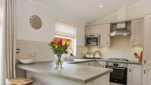 A modern kitchen with a central island, bar stools, a clock, and a window with blinds. - Kirkstone Lodge (Windermere)
