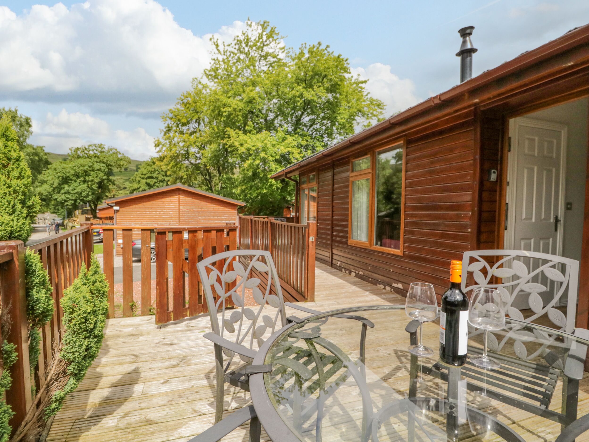 A wooden cabin with a glass table and chairs, a bottle of wine, and a wooden deck.
