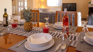 Un comedor con una mesa preparada para dos personas, con un centro de mesa de piña, una botella de vino tinto y una vela.