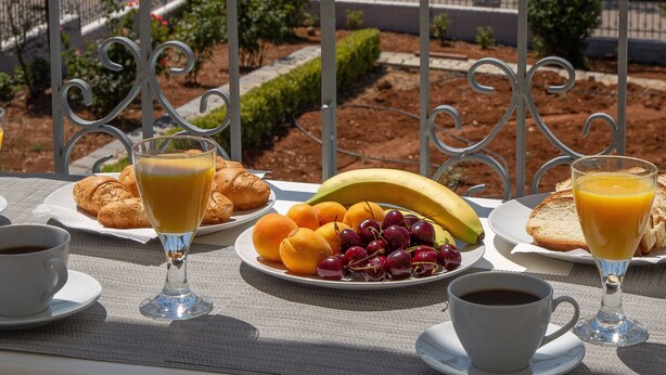 Una mesa de desayuno con cruasanes, fruta y café, con vistas a un paisaje pintoresco del mar y las montañas.