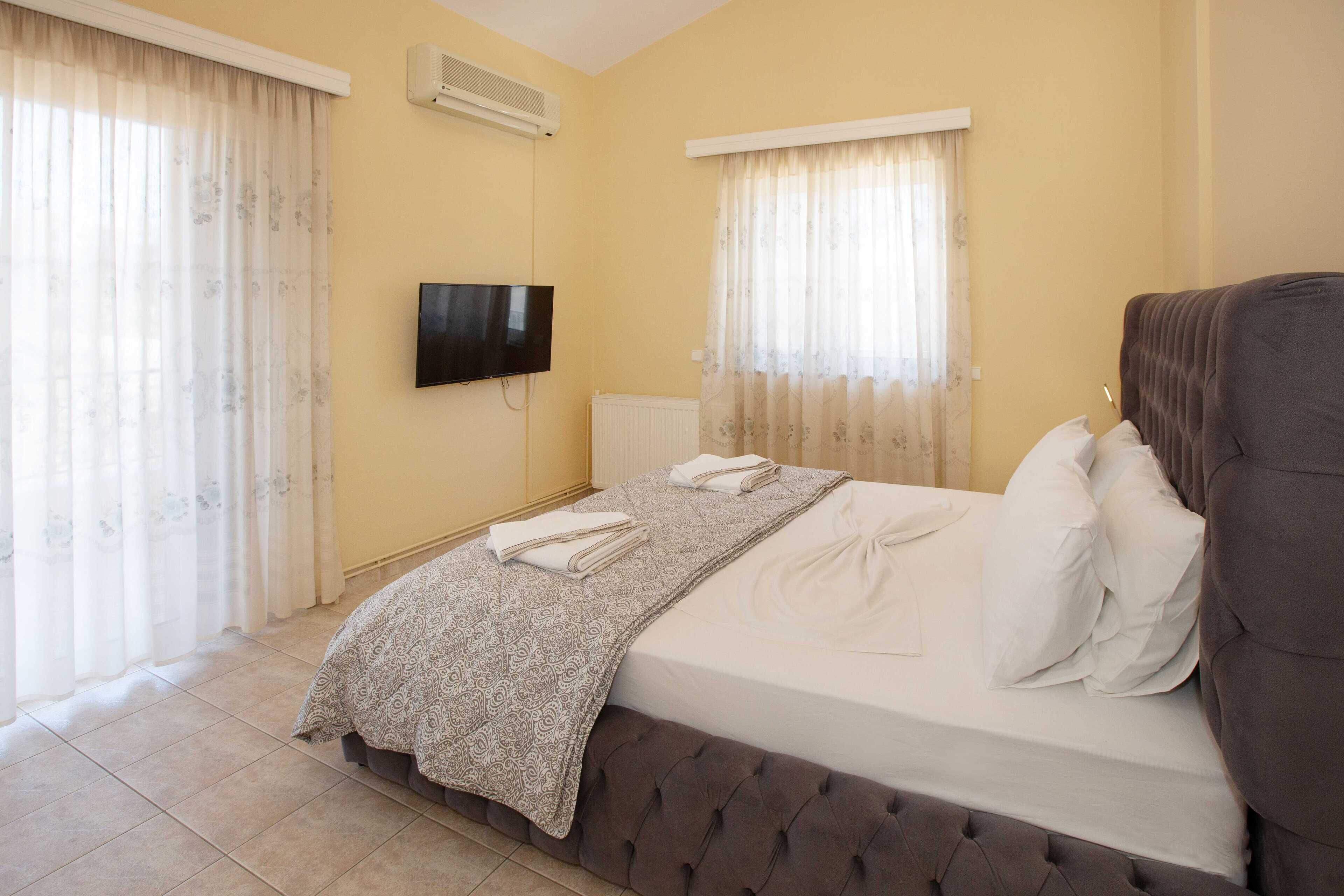 Une chambre d’hôtel avec un lit, un téléviseur fixé au mur et deux fenêtres avec des rideaux.