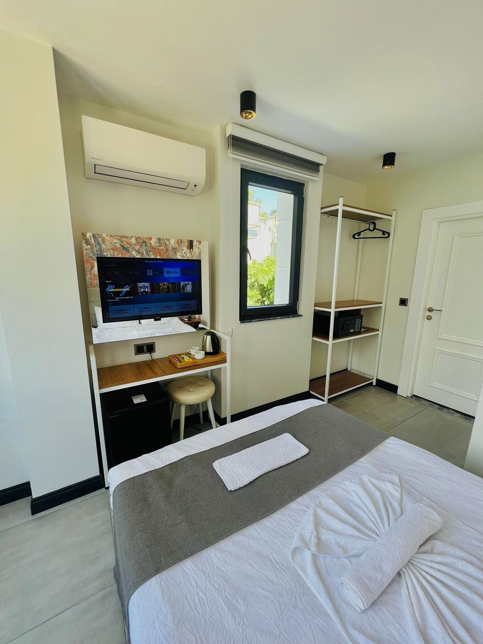 A compact hotel room with a bed, a desk with a computer, a window, and a wardrobe.