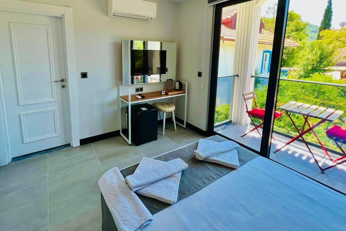Moderni huone, jossa on taulutelevisio, työpöytä ja parveke, jossa on punaiset tuolit.