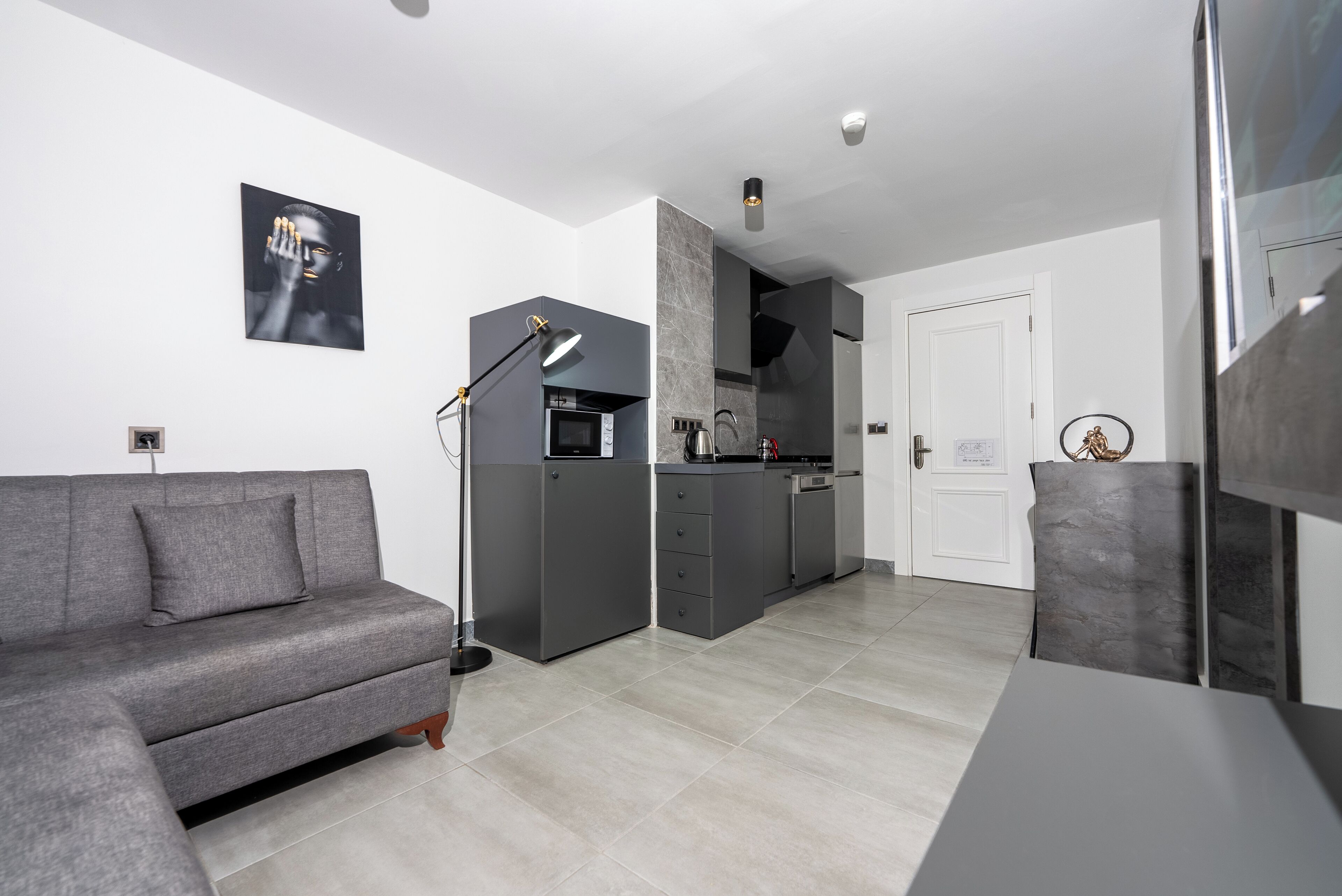 Un espacio habitable moderno y funcional con sofá gris, kitchenette y zona de comedor.