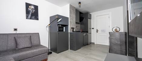 Un espacio habitable moderno y funcional con sofá gris, kitchenette y zona de comedor.