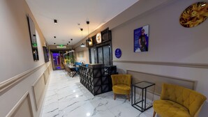 A hotel lobby with a marble floor, yellow armchairs, a reception desk, and wall art. - EURONOVA HOTEL & SUITES (Kemer)
