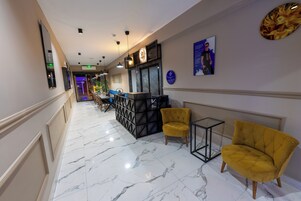 Un vestíbulo de hotel con suelo de mármol, sillones amarillos, un mostrador de recepción y obras de arte en las paredes.