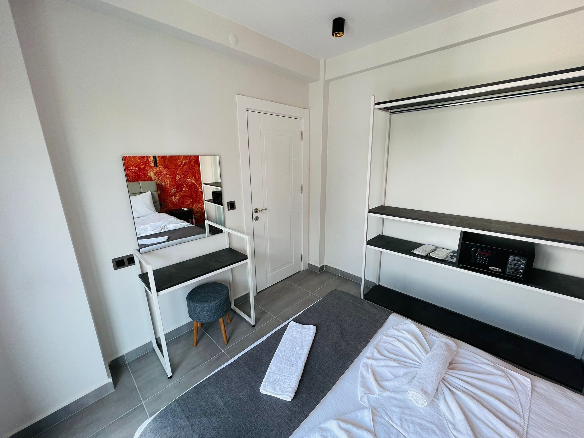 A modern hotel room with a bed, a desk with a chair, a wardrobe, and a built-in TV.