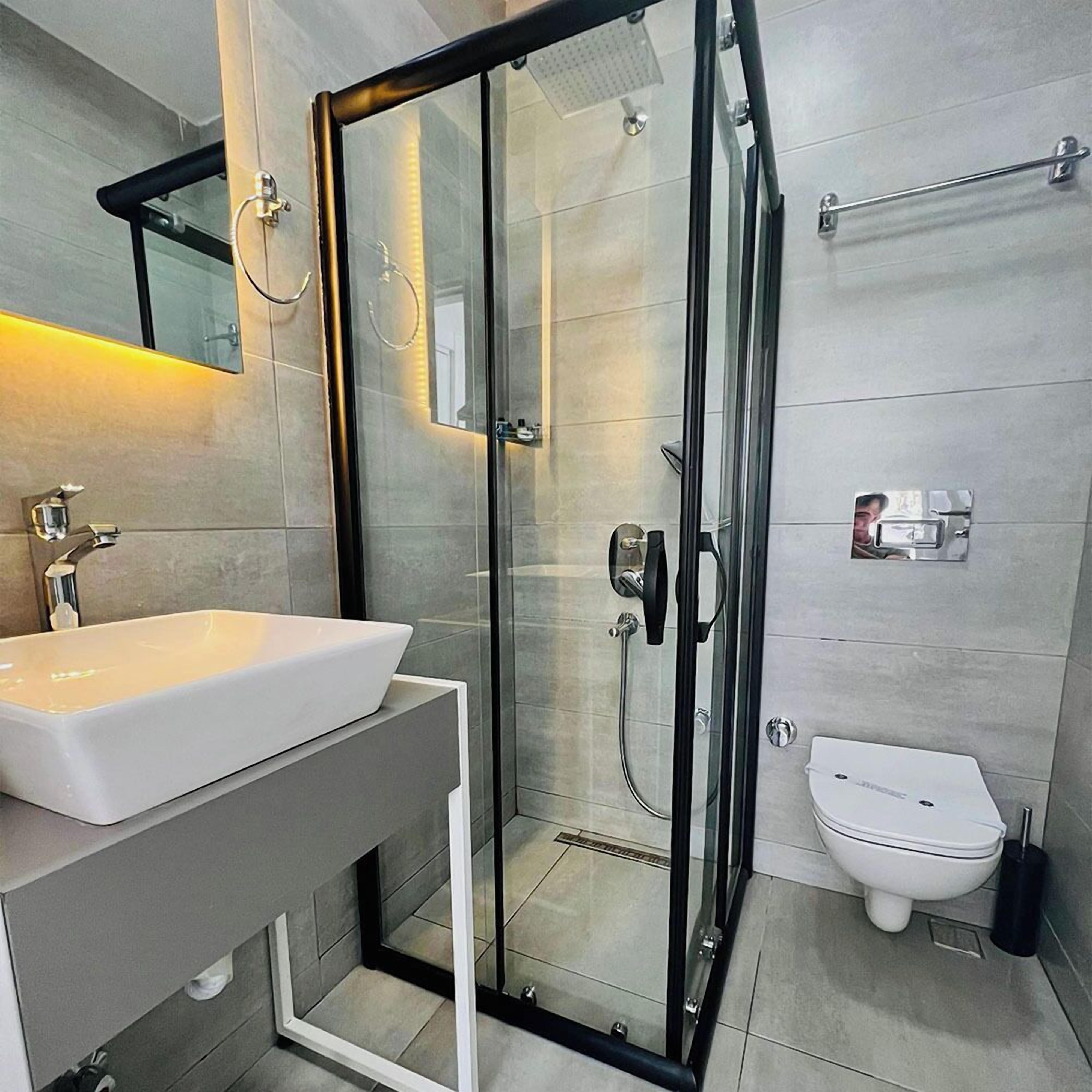 A modern bathroom with a glass-enclosed shower, a white sink, and a toilet.