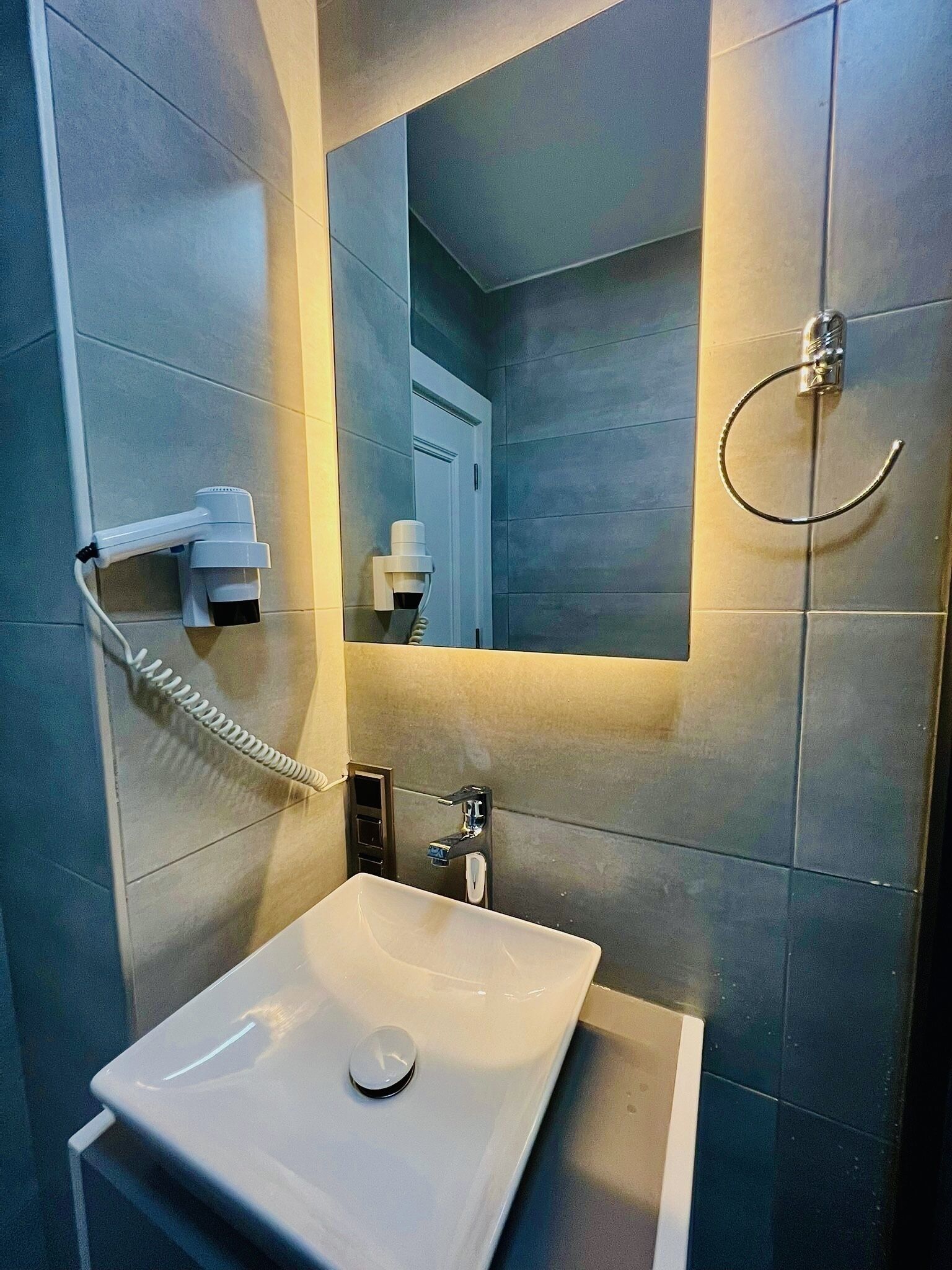 Un baño moderno con un lavamanos blanco, un cabezal de ducha de mano y un perchero.