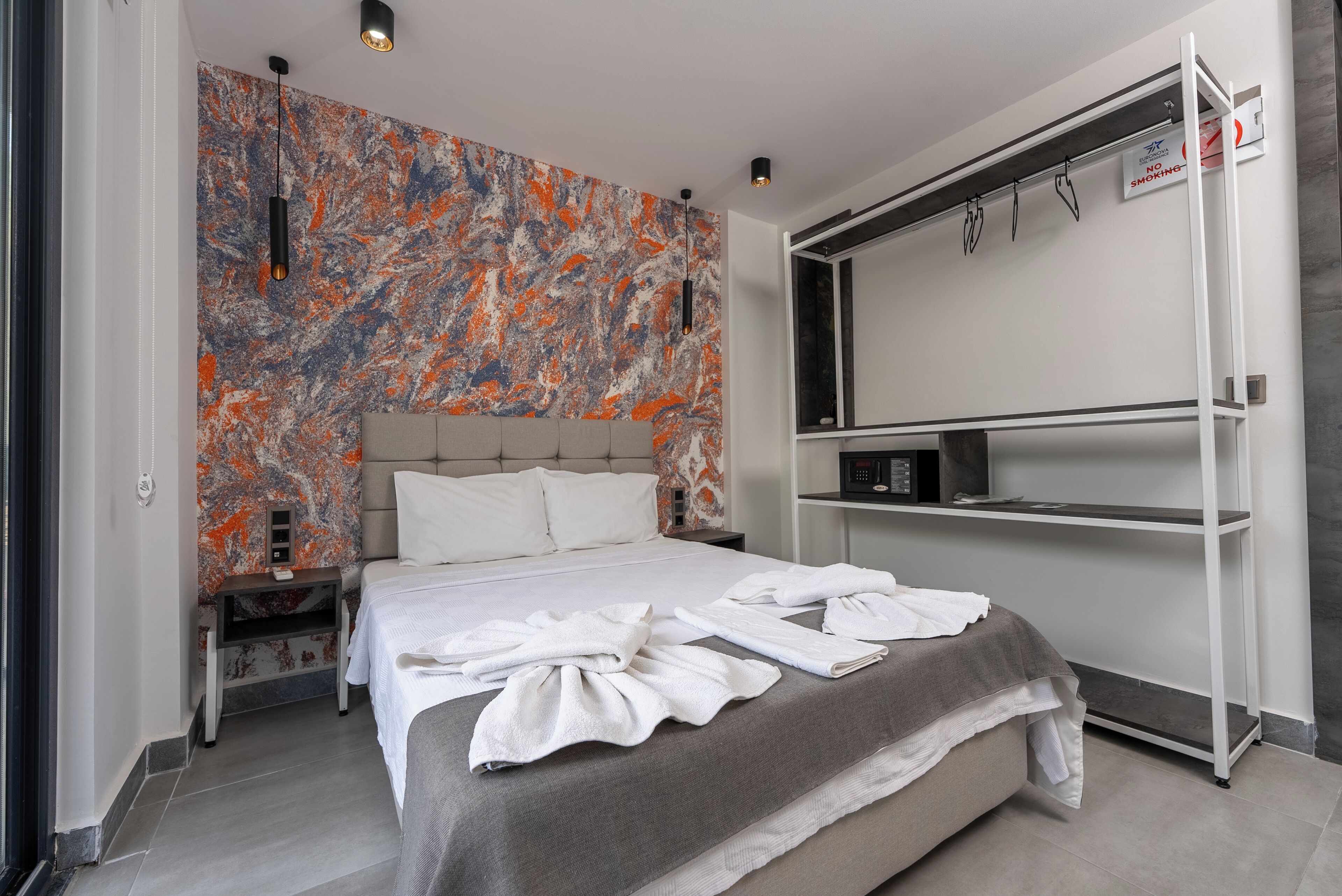 Moderni hotellihuone, jossa on suuri sänky, marmorikuvioitu korosteseinä, yöpöytä ja sisäänrakennettu TV-taso.