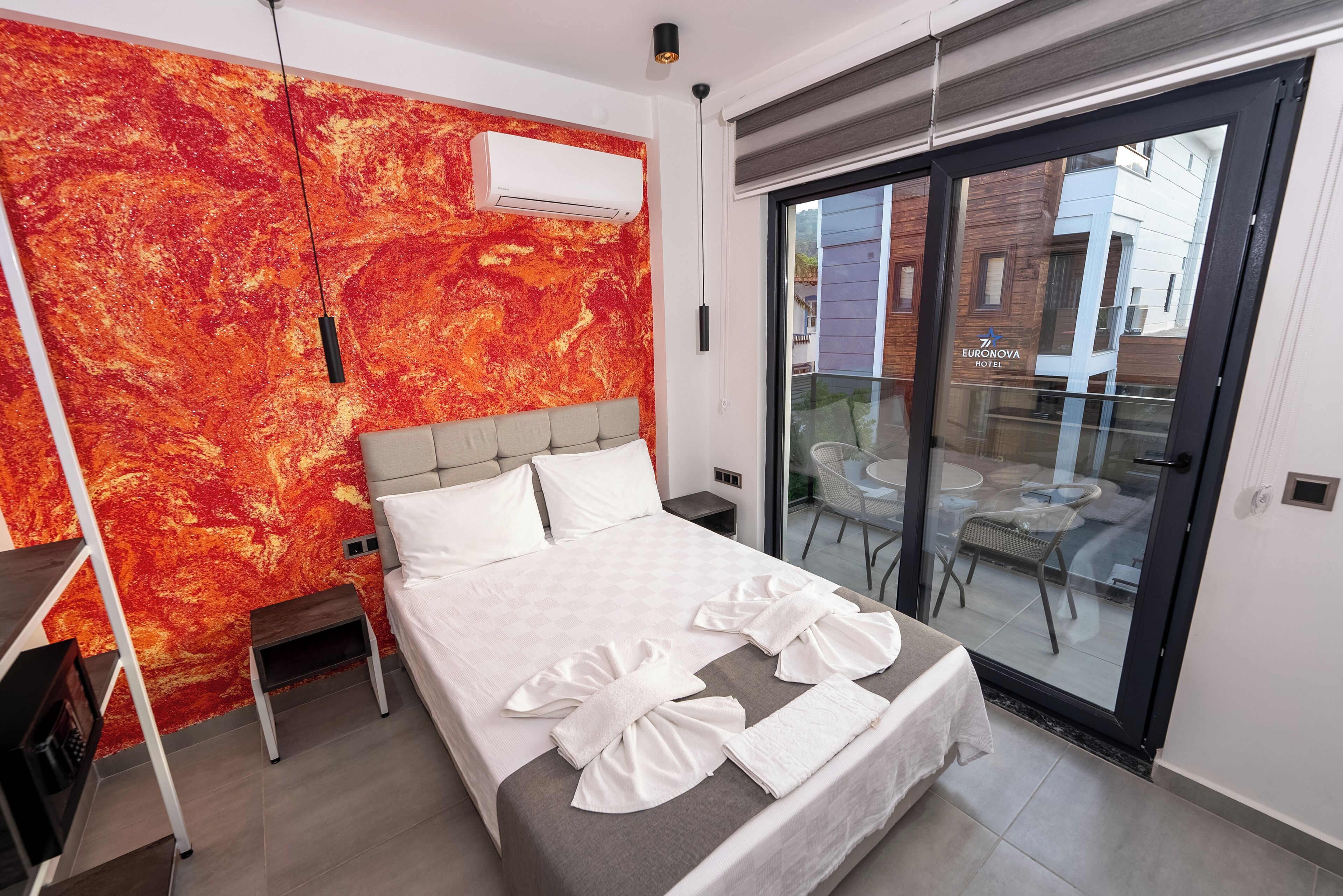 Una habitación de hotel moderna con una cama grande, un pared de diseño abstracto rojo y una puerta corrediza de vidrio al exterior.
