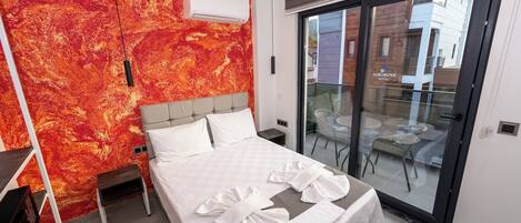 Una habitación de hotel moderna con una cama grande, un pared de diseño abstracto rojo y una puerta corrediza de vidrio al exterior.