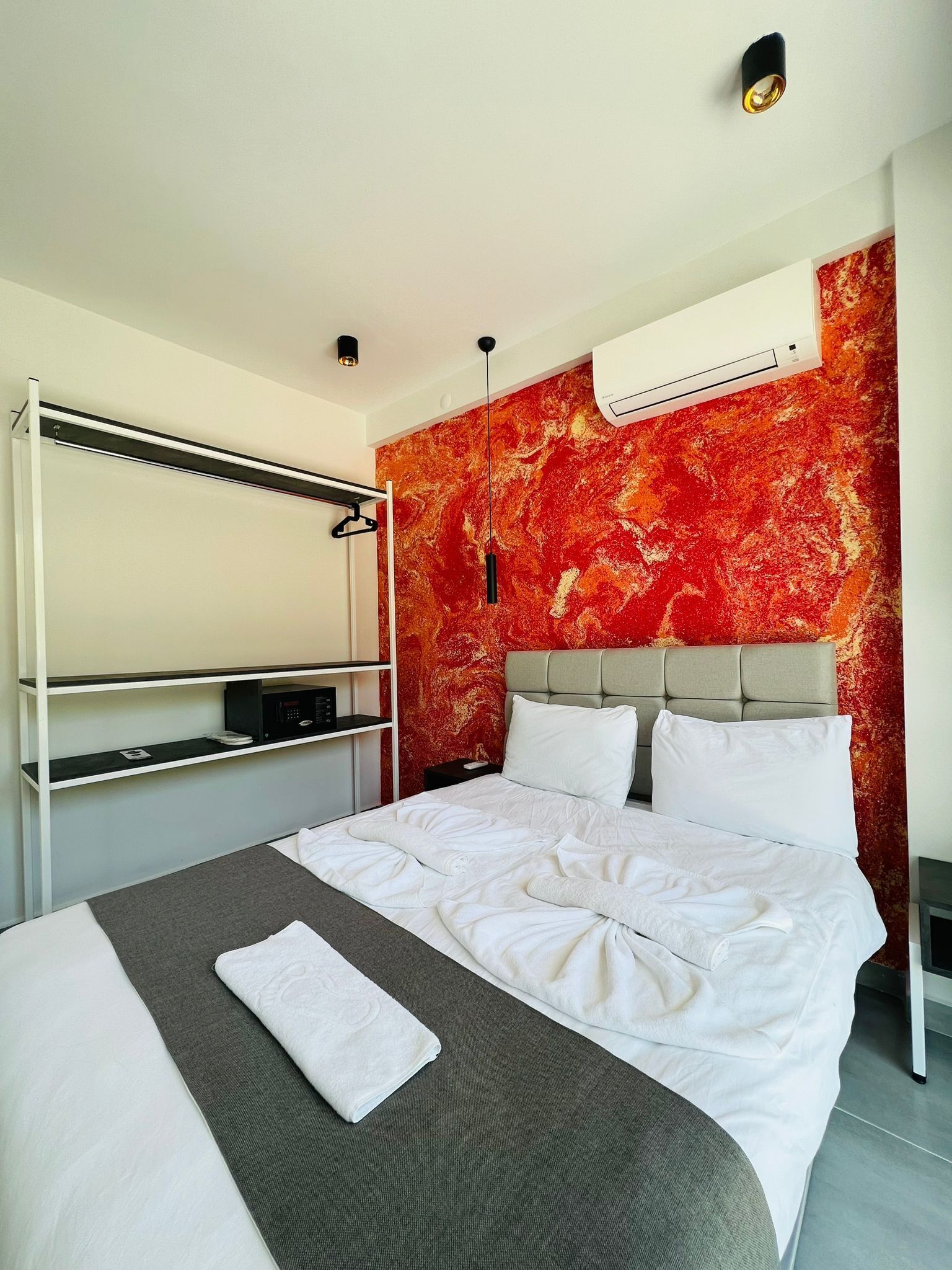 Une chambre d’hôtel avec un lit, une armoire intégrée, un mur décoré d’un motif rouge et un climatiseur fixé au plafond.