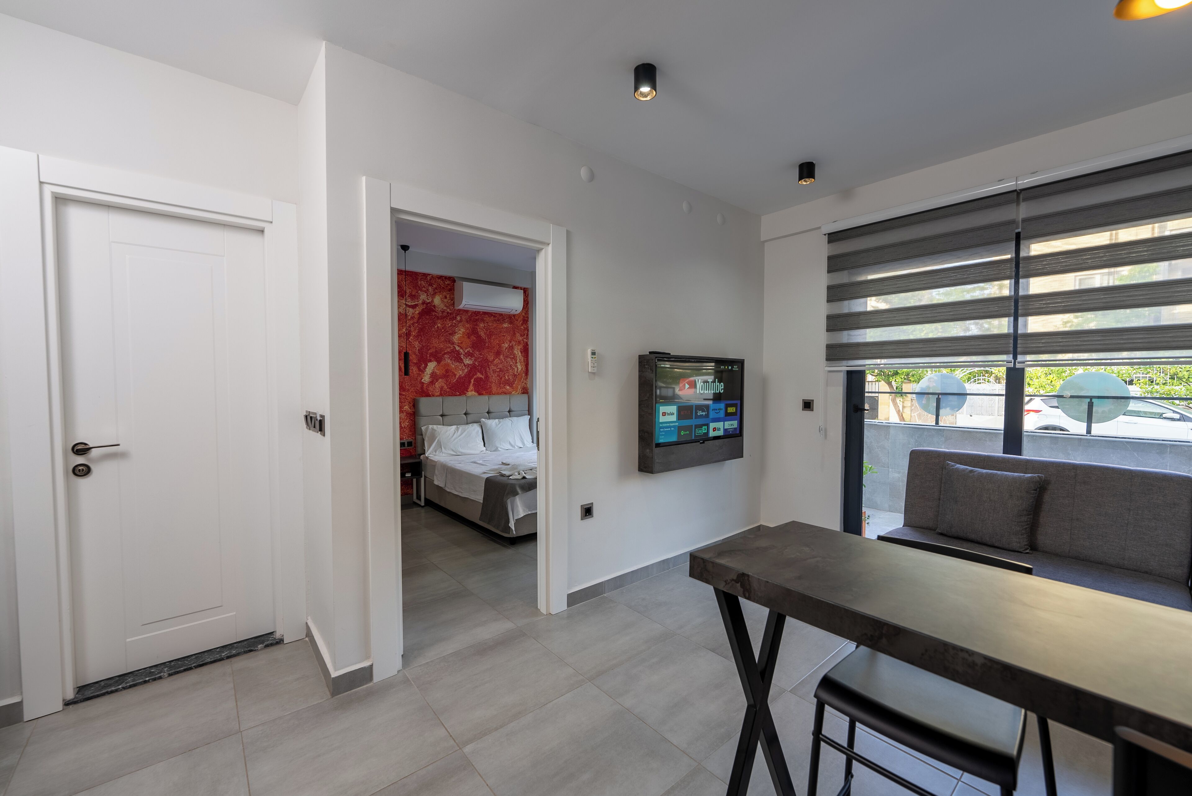 A modern hotel room with a bed, a TV, and a seating area by the window.