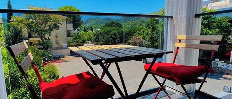 A balcony with a table and two chairs, overlooking a scenic landscape with greenery and buildings.