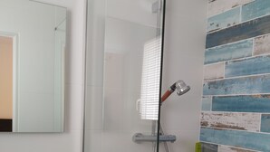 Un baño moderno con cabina de ducha de vidrio, un lavamanos blanco y una pared decorada con azulejos.