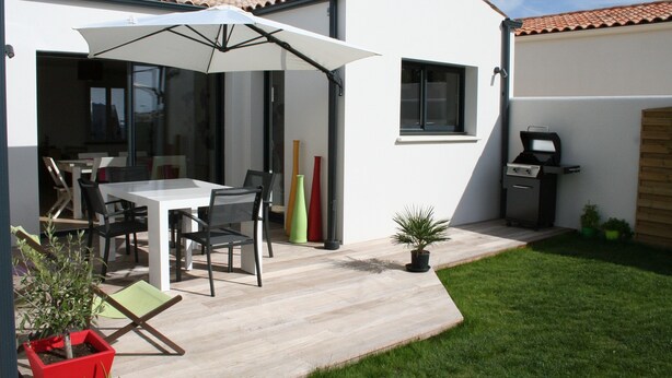 Un patio al aire libre con una mesa, sillas, una parrilla y plantas en macetas.