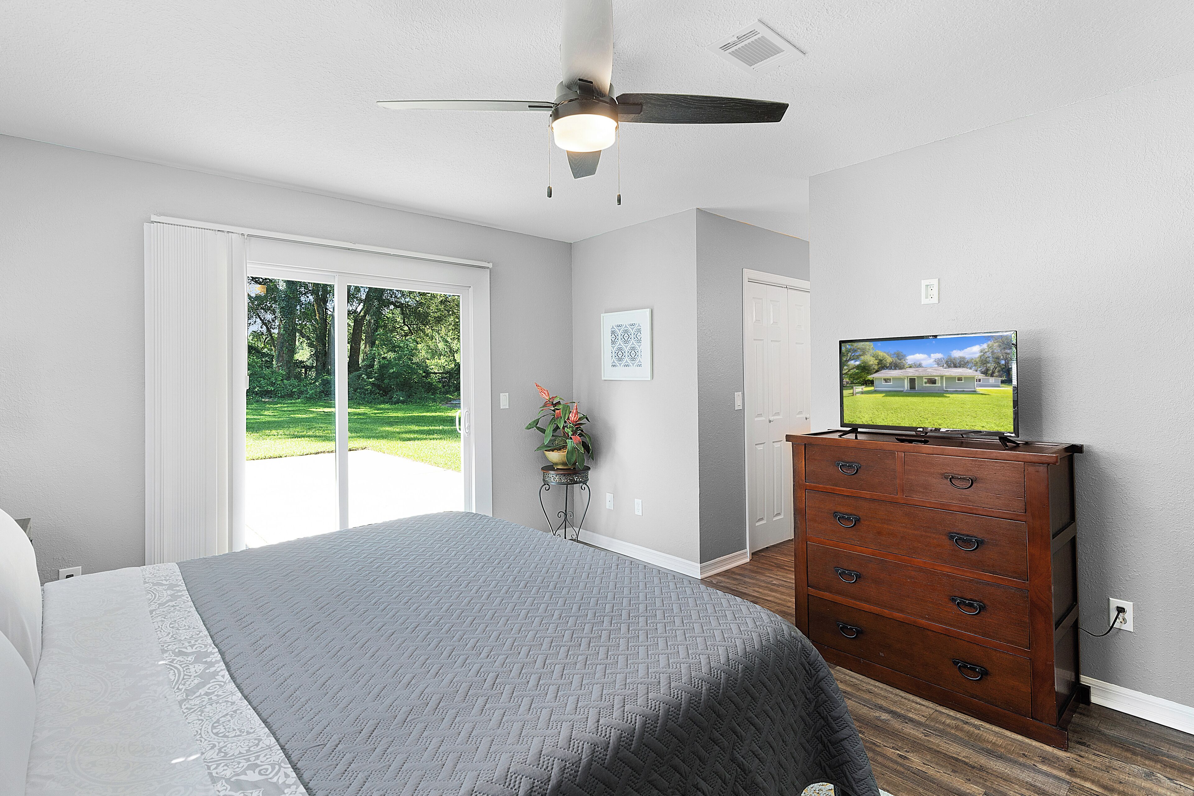 Une chambre à coucher avec un lit, une commode, un ventilateur de plafond et un téléviseur posé sur la commode.