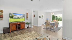 A modern living room with hardwood flooring, a flat-screen TV, a wooden entertainment unit, and a dining area with a table and chairs. - The Horseman's Retreat (Ocala)