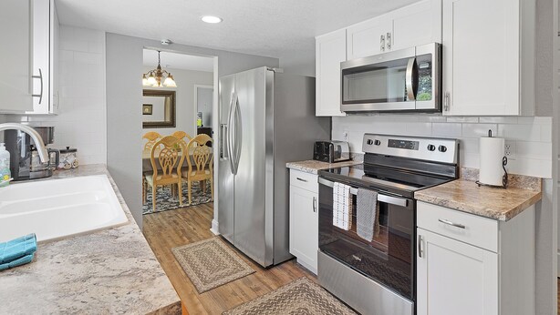 A modern kitchen with stainless steel appliances, white cabinetry, and a granite countertop. - The Horseman's Retreat (Ocala)