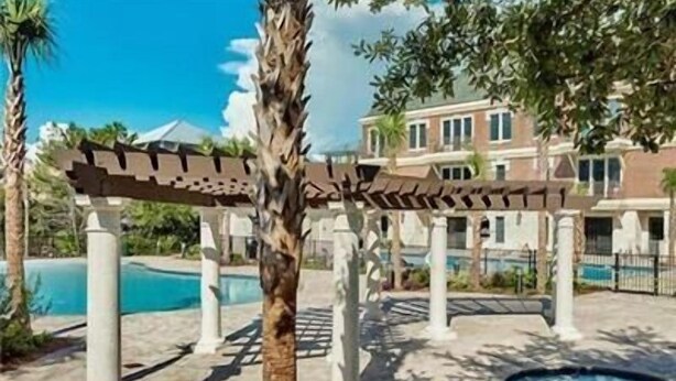 A pool area with a pergola, palm trees, and a building in the background.