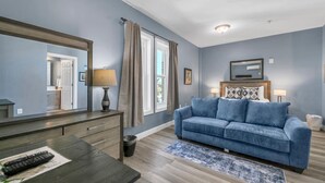 A room with a blue couch, a wooden dresser, a mirror, and a window with curtains.