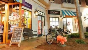 A storefront with a neon sign, a bicycle, and a pig statue.