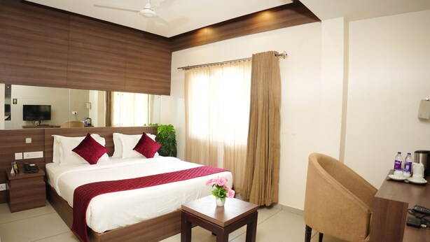 A modern hotel room with a large bed, a desk, a chair, a TV, and a ceiling fan. - Hotel Palmyra Grand Inn (Kanayannur)
