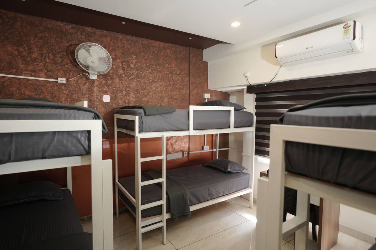 A dormitory room with bunk beds, a wall-mounted fan, and an air conditioning unit.
