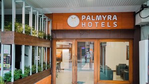 The exterior of Palmyra Hotels with a wooden facade, glass doors, and a green entrance mat. - Hotel Palmyra Grand Inn (Kanayannur)