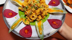 A plate of food with various garnishes and a central dish, held over a table. - Hotel Palmyra Grand Inn (Kanayannur)