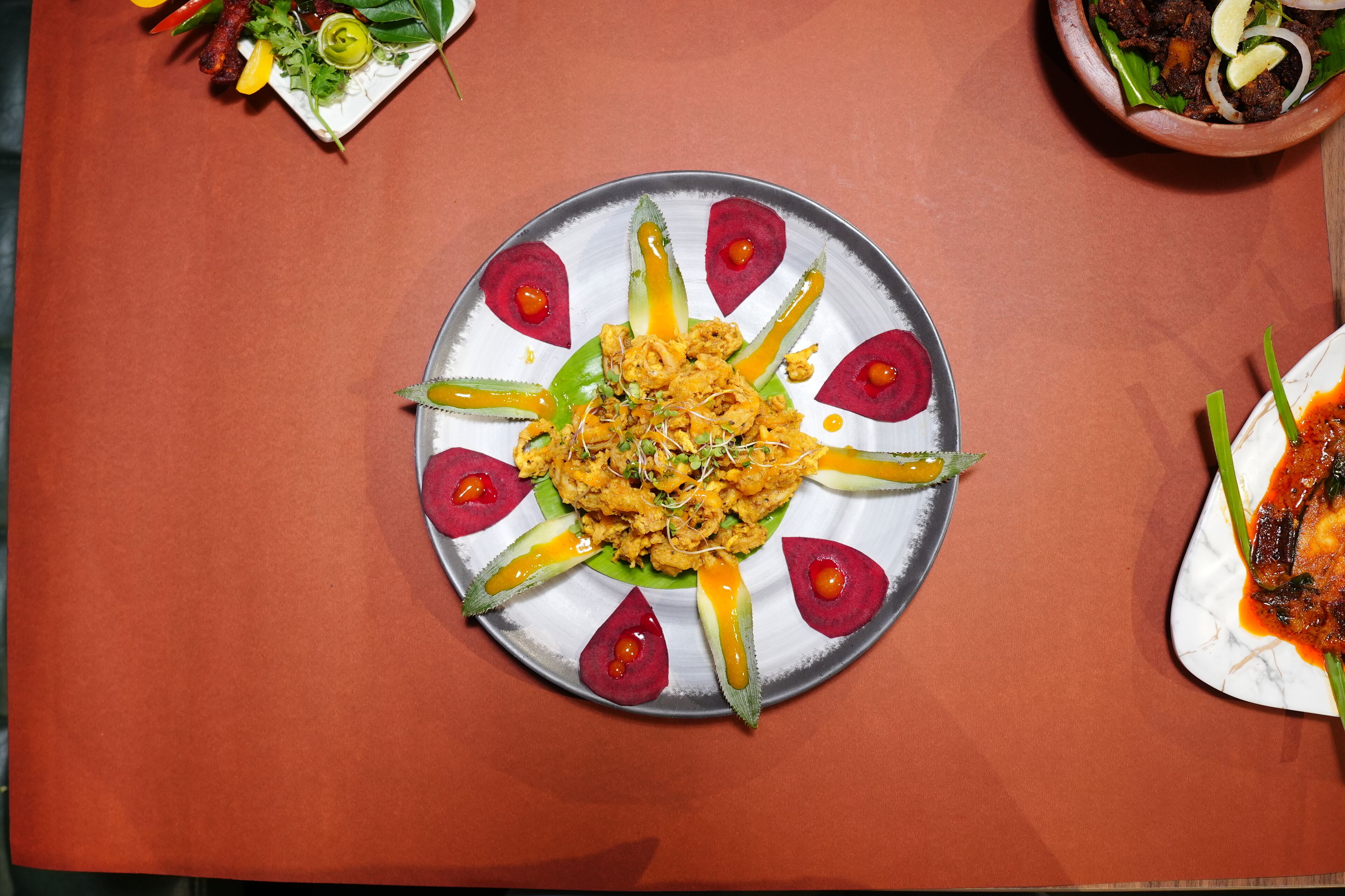 A dining table with a variety of dishes, including a central plate with a colorful arrangement of food and garnishes.