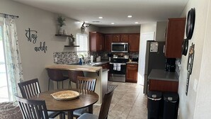 A modern kitchen with wooden cabinets, a central island, and a dining area with a round table and chairs. - AZ Sun & Serenity: 4BR home w/Heated Pool, BBQ Island, Prime location– Sleeps 12 (Surprise)